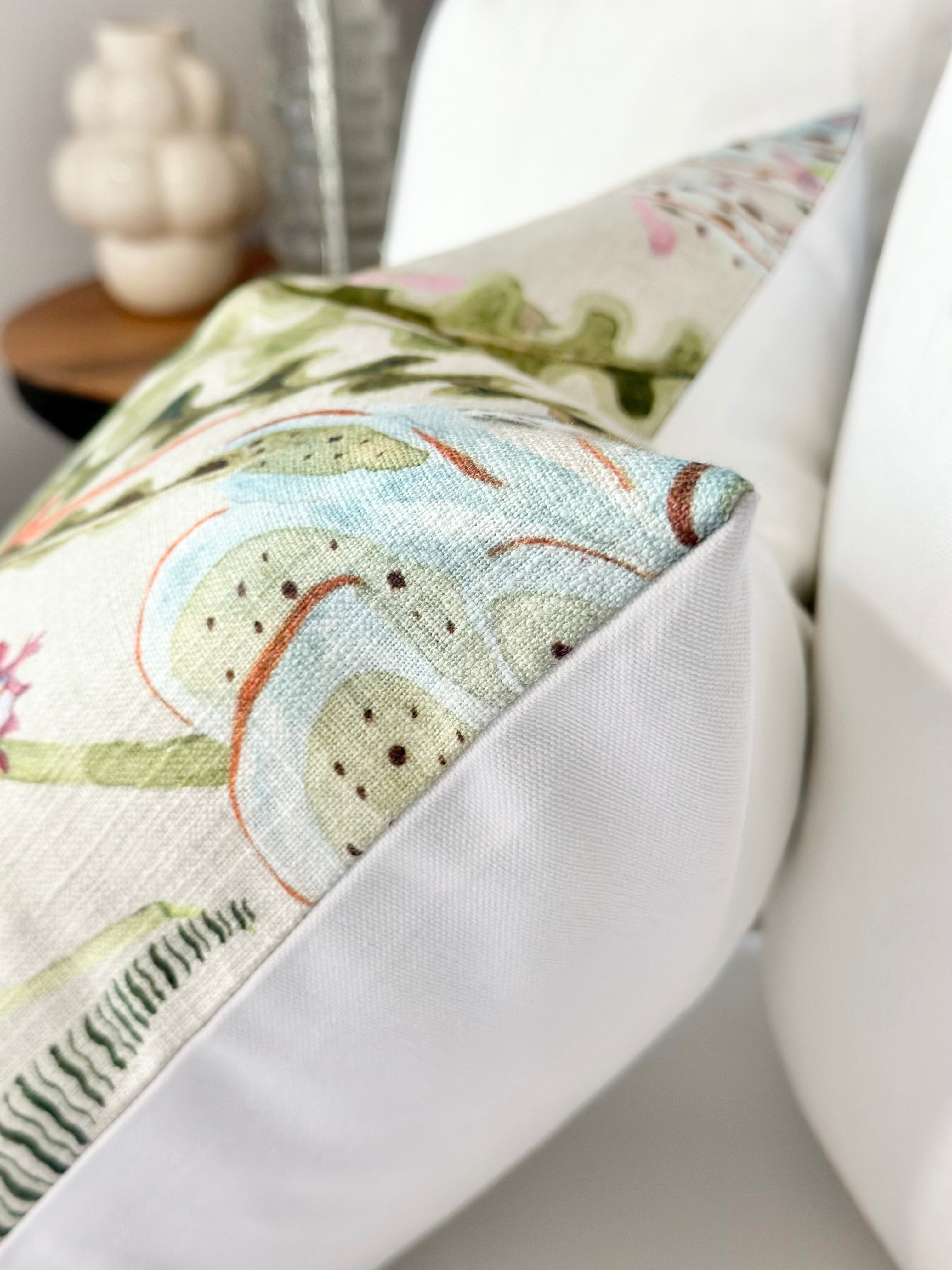 Close-up of a luxury throw pillow cover showcasing a pastel coral pattern with seaglass, blush, and green colors on the front. The back is crafted from high-quality Schumacher cotton canvas, and the cover is made-to-order with an invisible zipper for a polished look. Ideal for enhancing stylish home accents and contemporary interiors