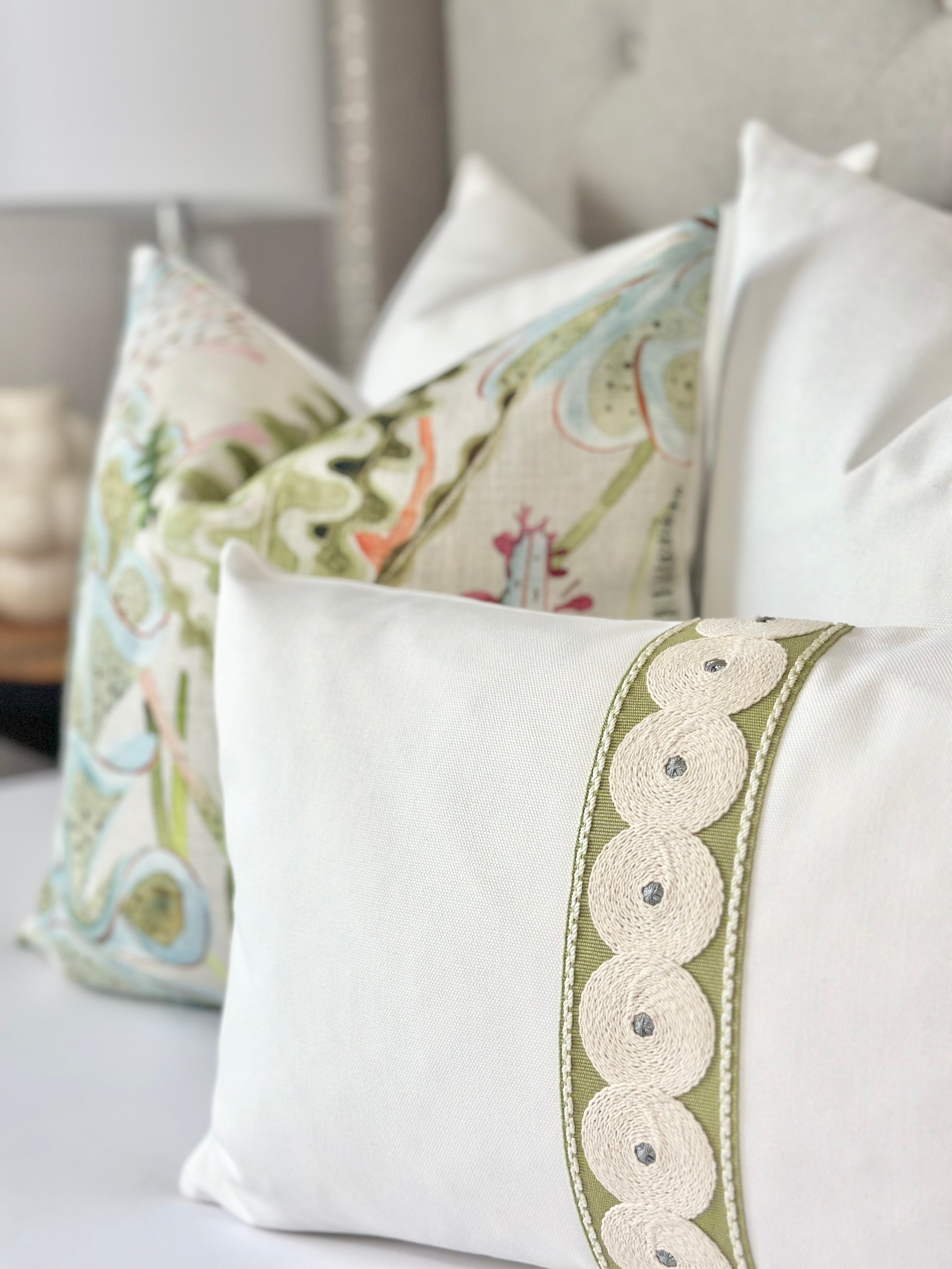 Close-up of a luxury pillow cover featuring white Schumacher fabric with olive green decorative tape and beige circular thread detailing. This designer pillow is custom-made for contemporary decor, showcasing intricate craftsmanship and high-quality materials that enhance the aesthetic of modern spaces